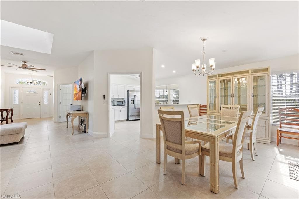 Tiled dining area featuring ceiling fan with notable chandelier, plenty of natural light, and a skylight