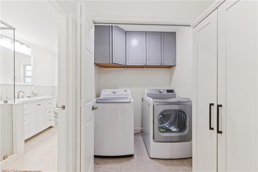 Laundry area with light tile patterned floors, sink, separate washer and dryer, and cabinets