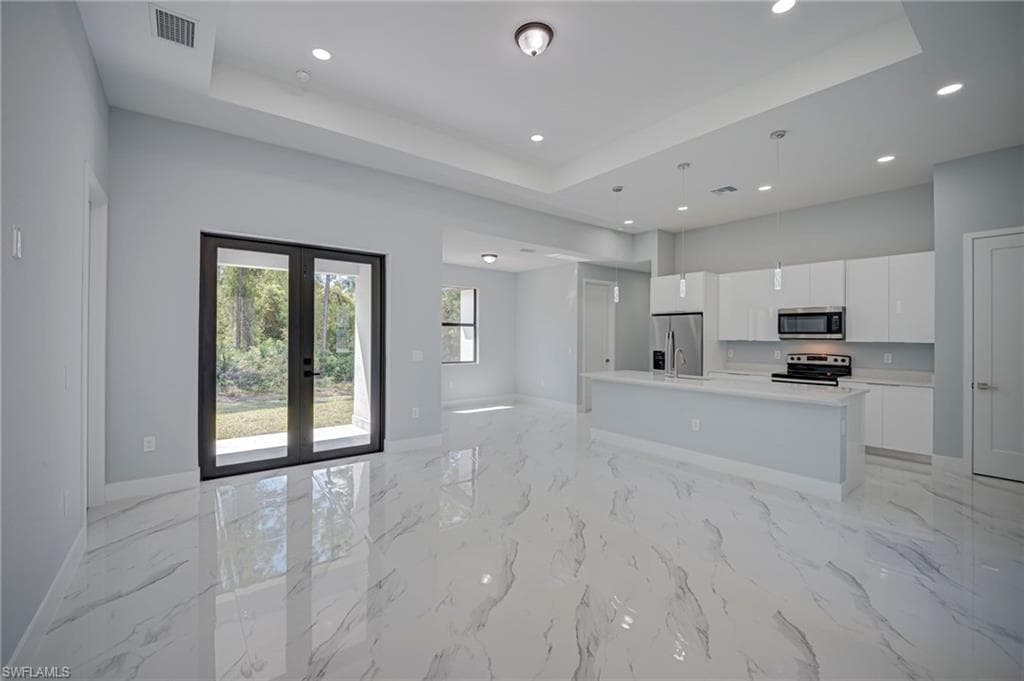 Kitchen featuring open floor plan, white cabinetry, an island with sink, french doors, and stainless steel appliances