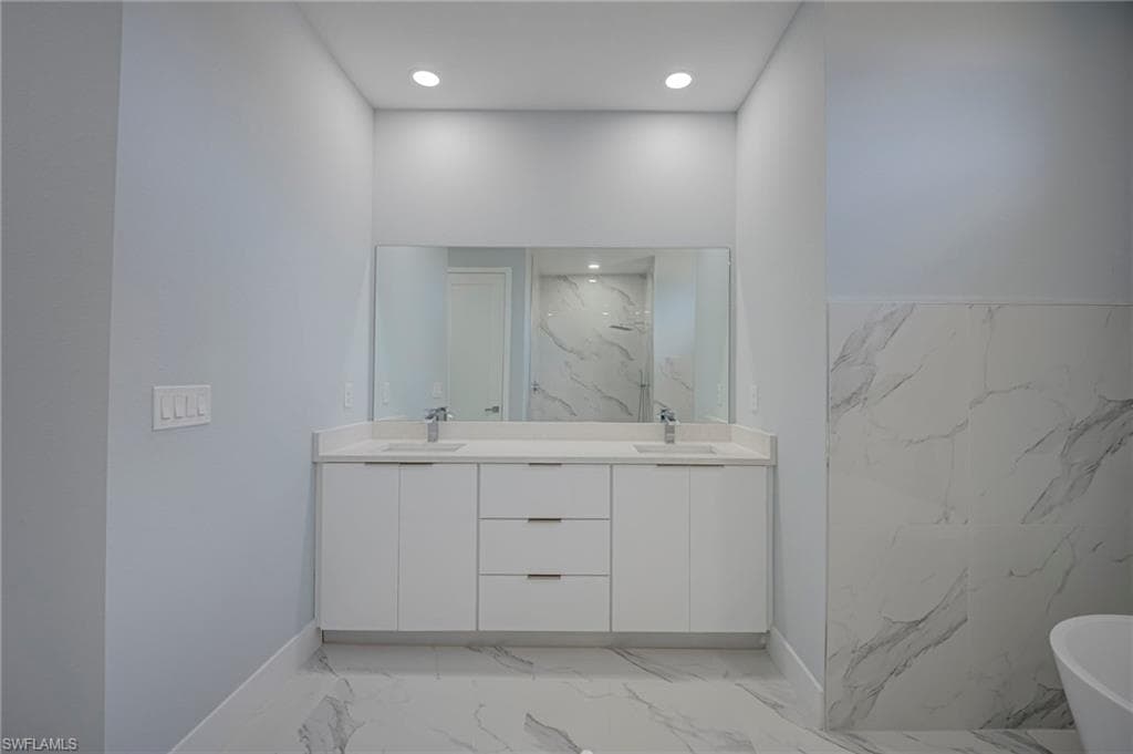 Full bath featuring a freestanding tub, double vanity, light marble finish floors, and recessed lighting