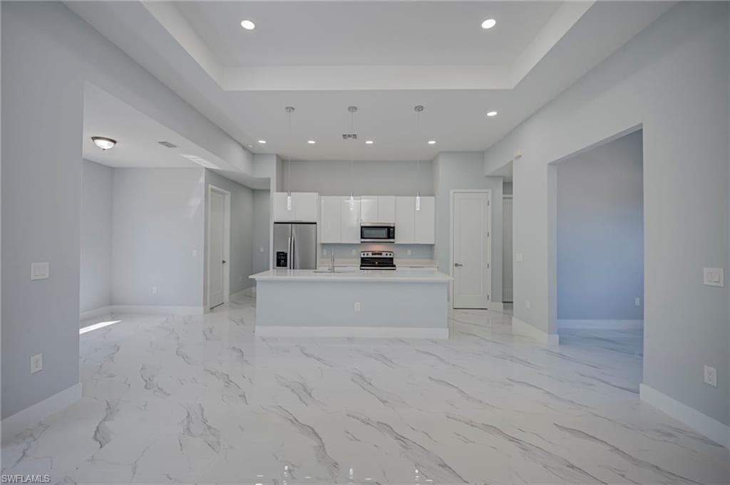 Kitchen with open floor plan, white cabinets, an island with sink, stainless steel appliances, and a raised ceiling