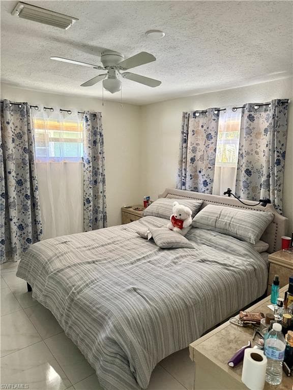 Tiled bedroom featuring multiple windows, a ceiling fan, and a textured ceiling