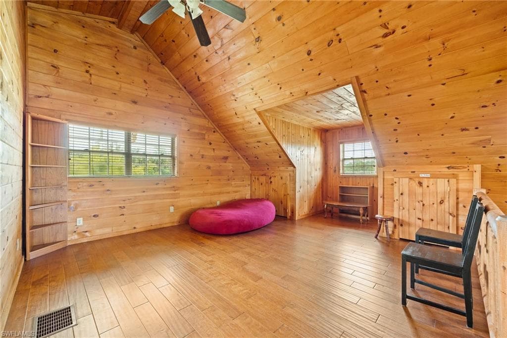 Bonus room with wood walls, a vaulted wooden ceiling, hardwood / wood-style flooring, and a ceiling fan