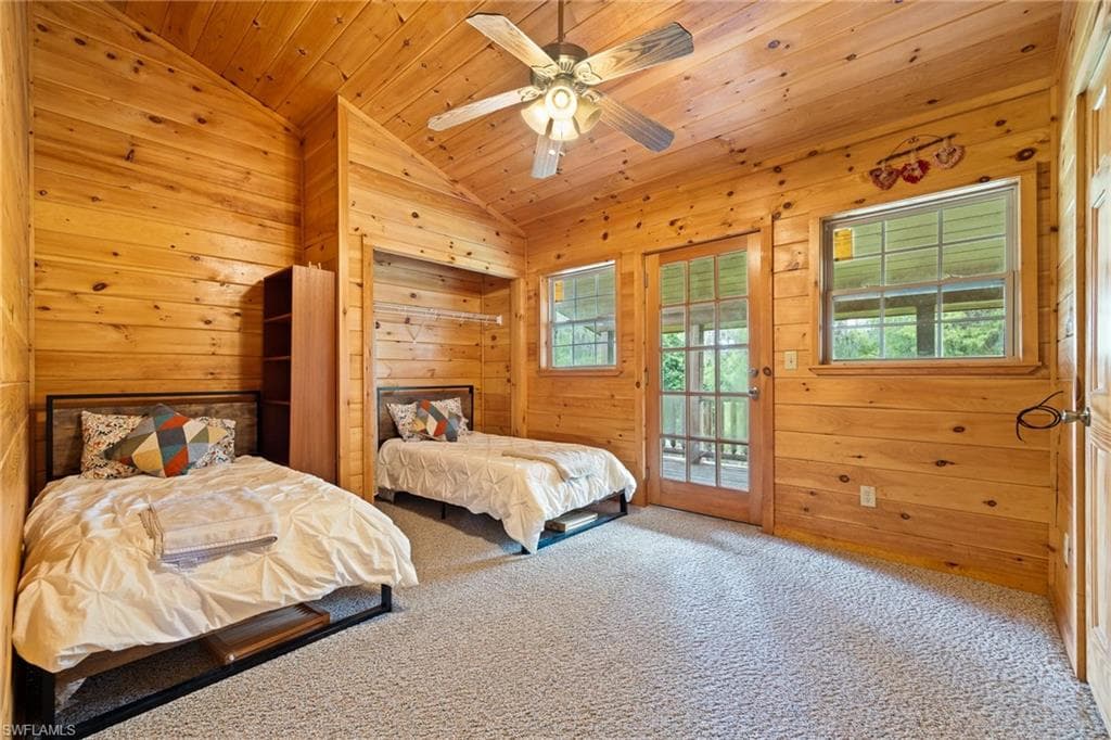 Carpeted bedroom featuring wood walls, access to outside, ceiling fan, and a vaulted wooden ceiling