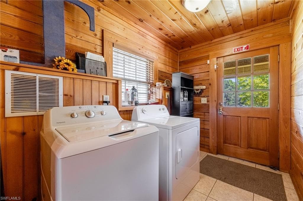 Laundry area with wood walls, wooden ceiling, light tile patterned floors, and separate washer and dryer