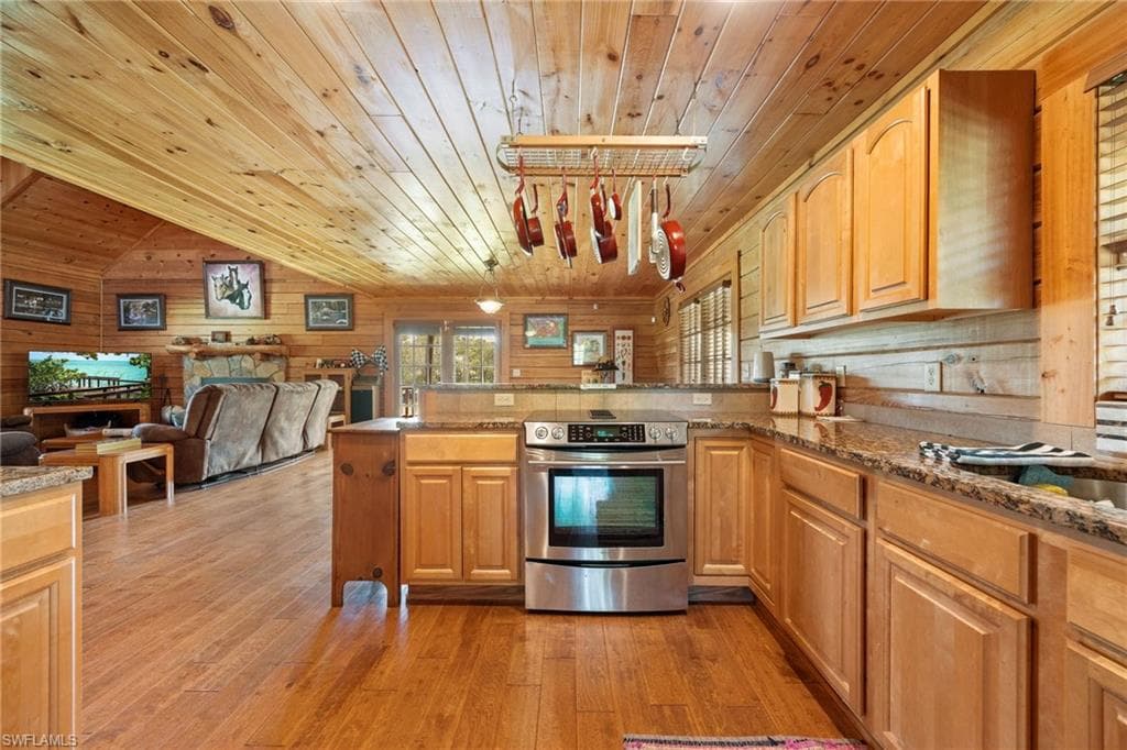 Kitchen with stainless steel electric range, a vaulted wooden ceiling, dark stone counters, light wood-style flooring, and open floor plan
