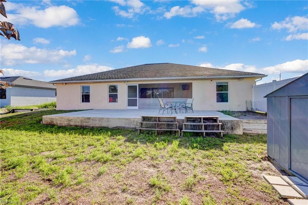 Back of house featuring a patio, stucco siding, a storage unit, and a lawn