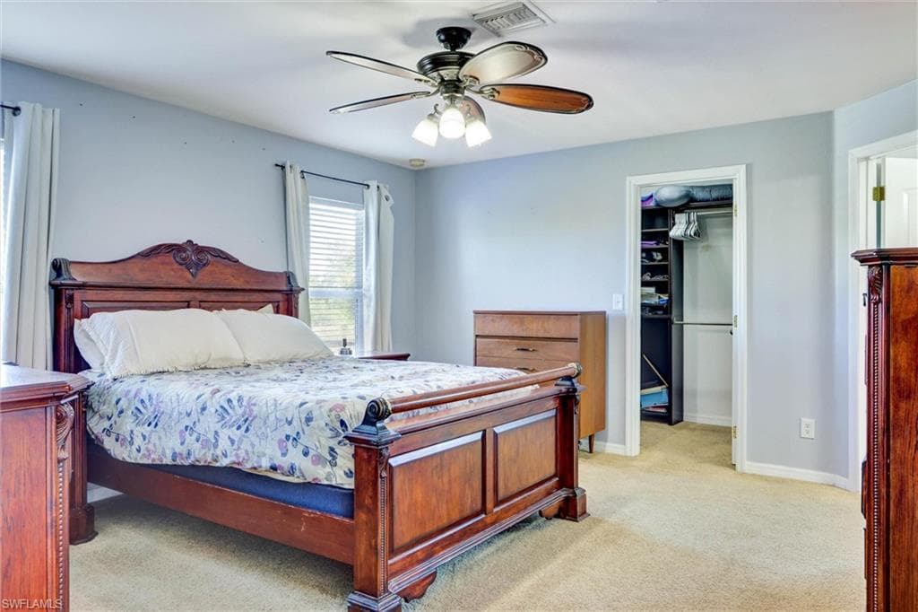 Bedroom with a walk in closet, light carpet, and a ceiling fan