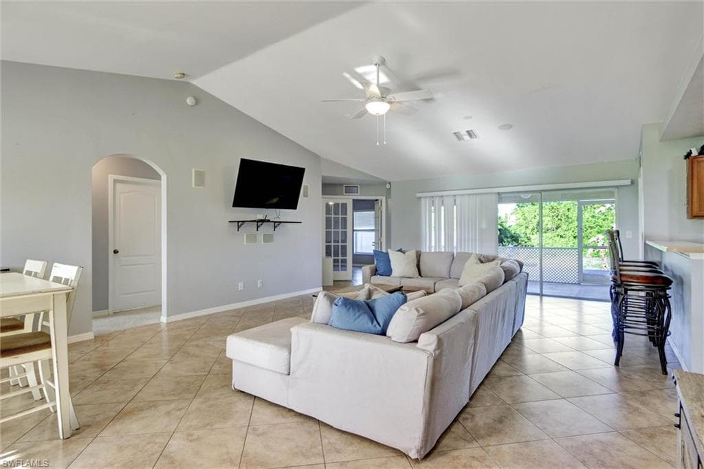 Living area with arched walkways, ceiling fan, light tile patterned flooring, a high ceiling, and plenty of natural light