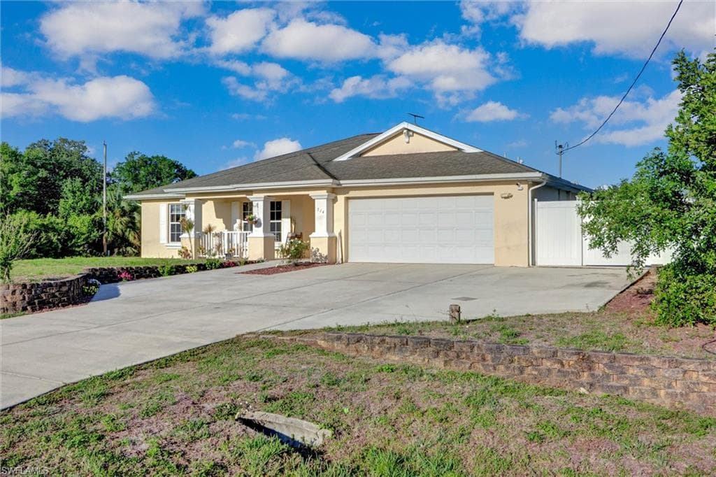 View of front facade featuring stucco siding, covered porch, an attached garage, and driveway