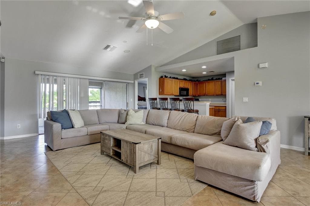 Living room with ceiling fan, light tile patterned flooring, and vaulted ceiling