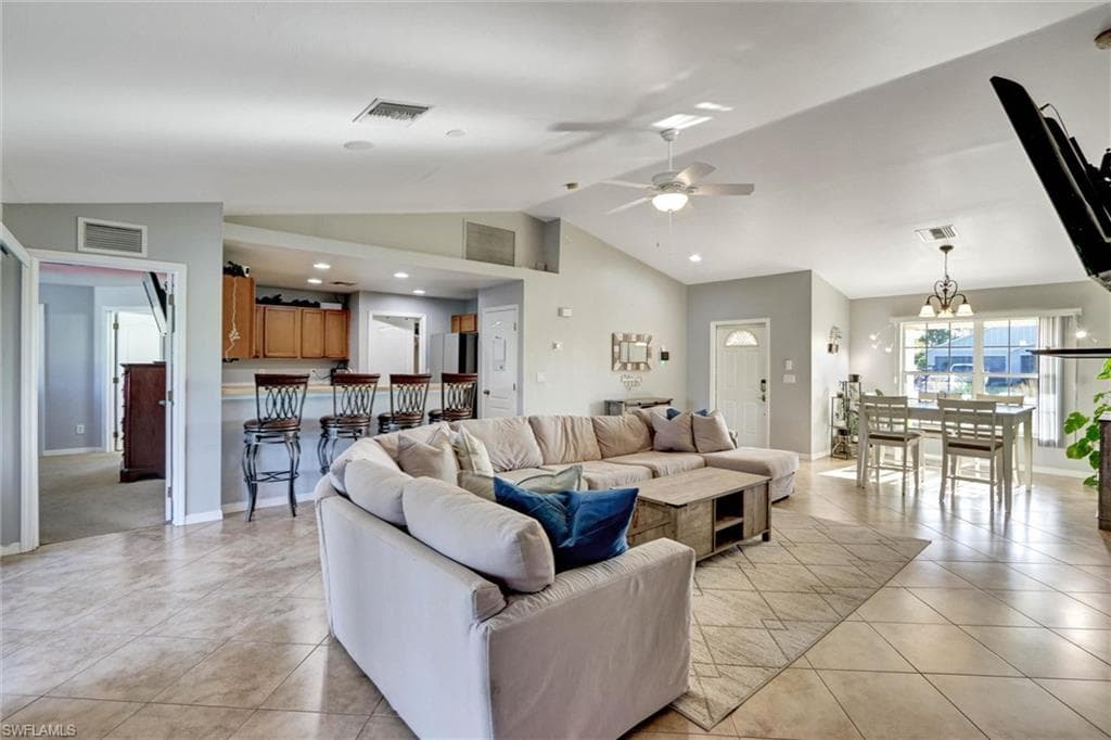 Living area with a ceiling fan, hanging lights, light tile patterned flooring, and a high ceiling