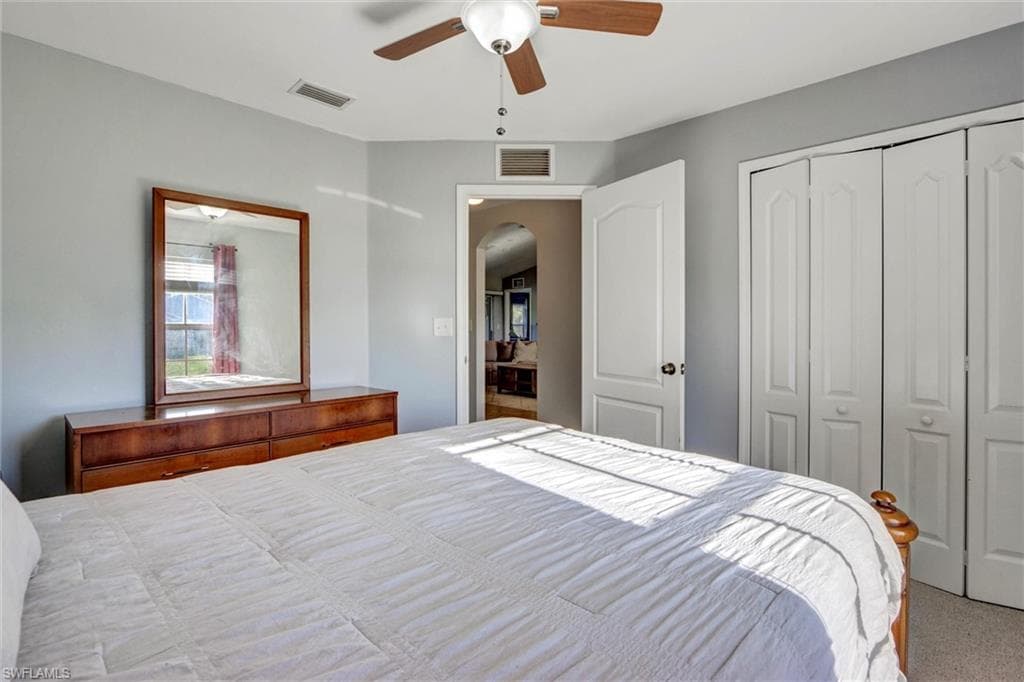 Carpeted bedroom with ceiling fan, a closet, and arched walkways