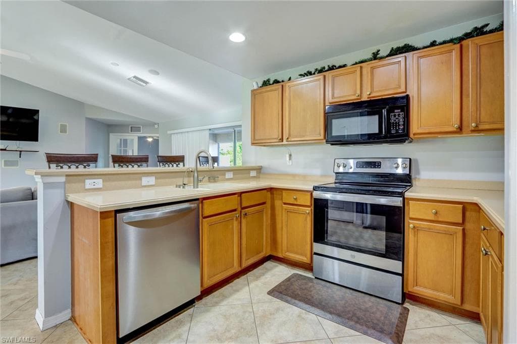 Kitchen featuring stainless steel appliances, light countertops, a peninsula, vaulted ceiling, and open floor plan