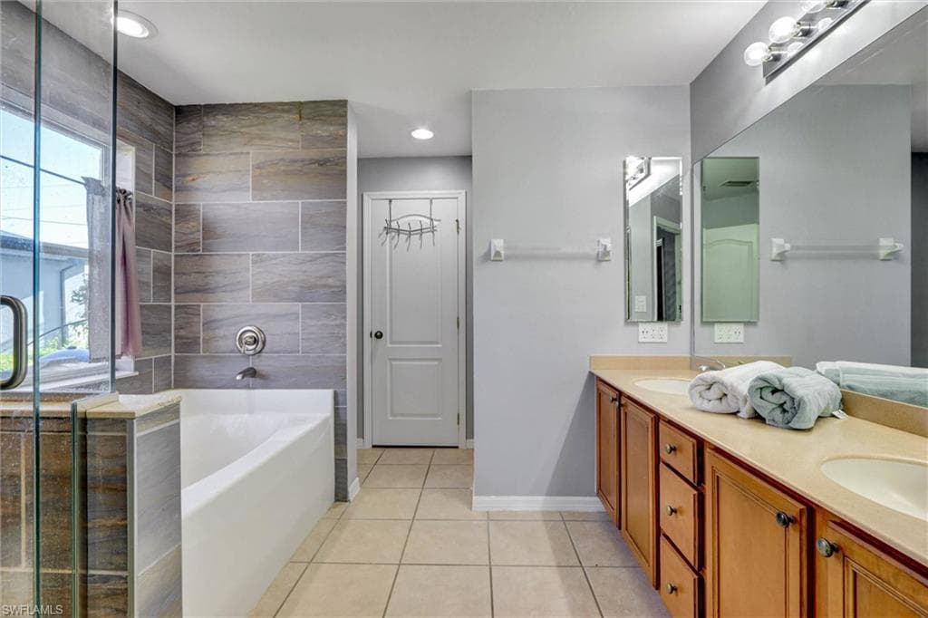 Full bathroom featuring double vanity, a stall shower, a garden tub, and light tile patterned floors