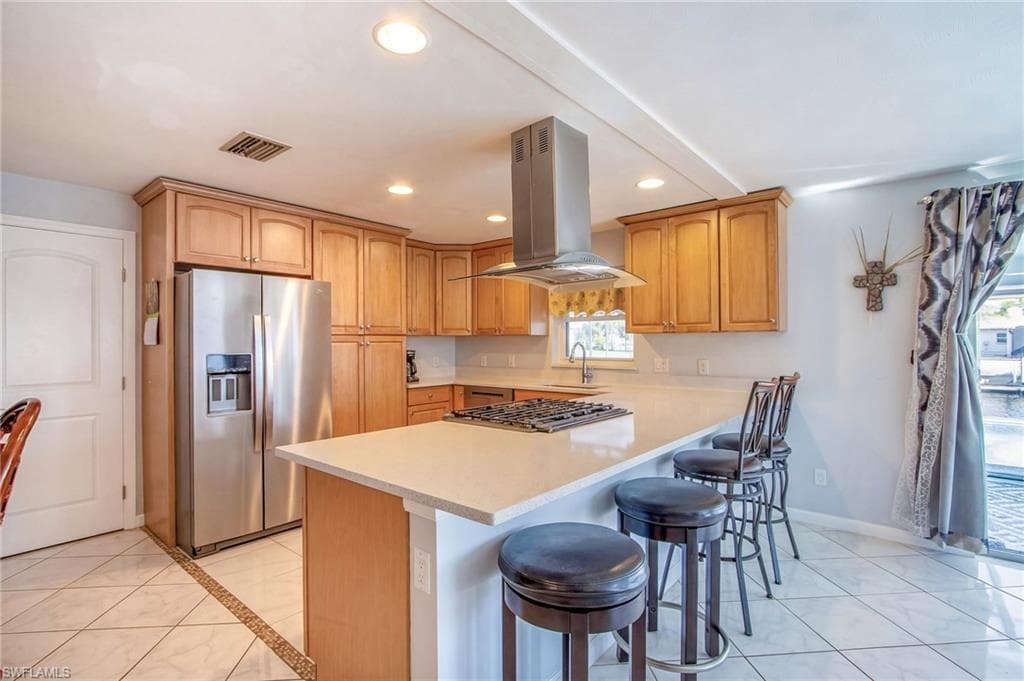 Kitchen with stainless steel refrigerator with ice dispenser, island range hood, a breakfast bar, light countertops, and recessed lighting