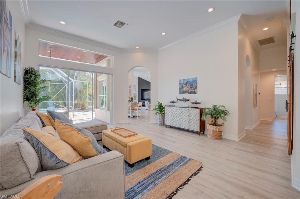 Living room with arched walkways, light wood-style flooring, crown molding, and recessed lighting