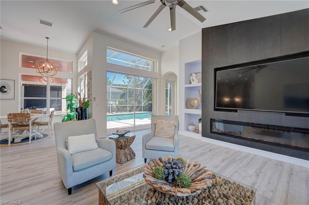 Living area with built in shelves, a ceiling fan, hanging lights, light wood-type flooring, and a sunroom