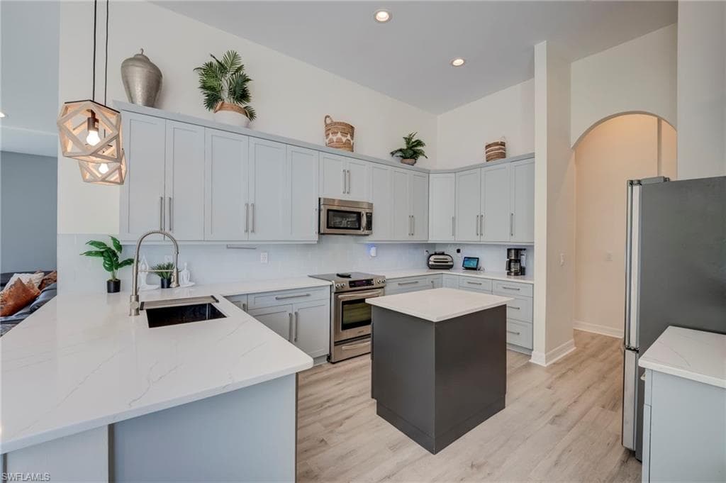 Two tone kitchen with stainless steel appliances, a peninsula, light wood finished floors, a kitchen island, and two tone cabinets