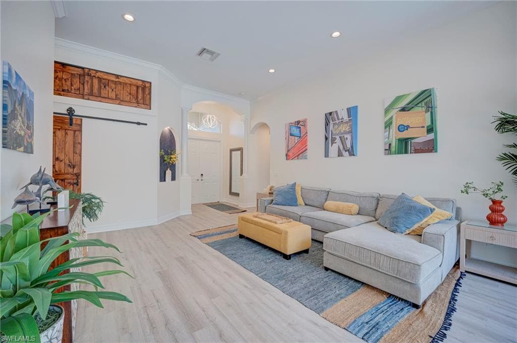 Living area featuring arched walkways, light wood finished floors, recessed lighting, and ornamental molding