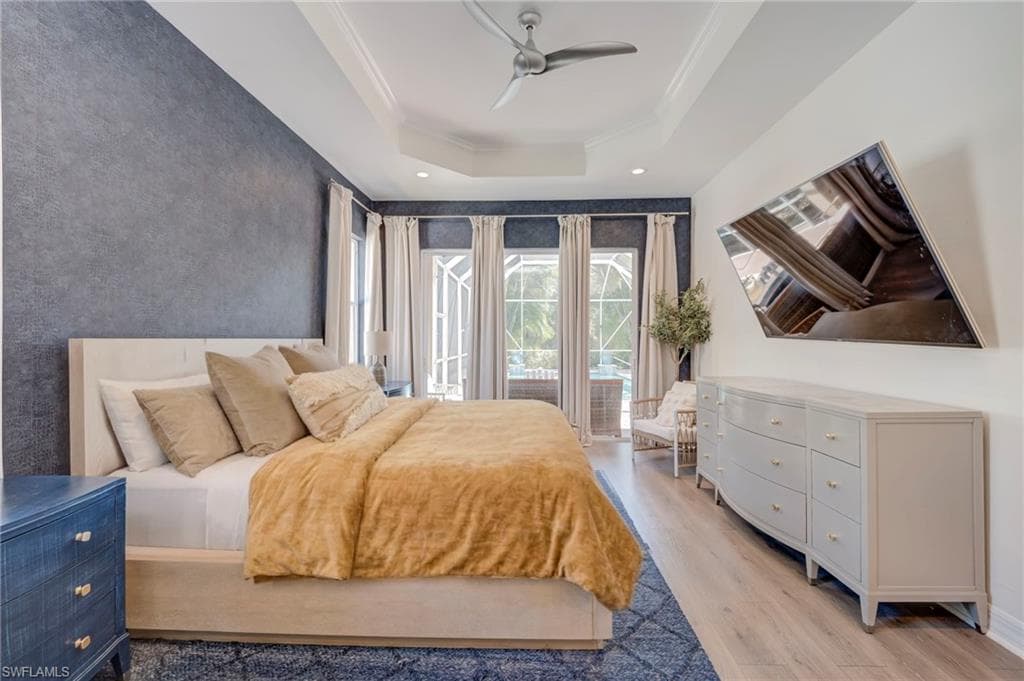 Bedroom with light wood-style floors, access to exterior, a ceiling fan, crown molding, and a raised ceiling