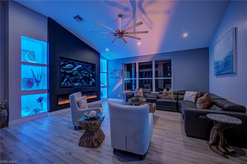 Living area featuring vaulted ceiling, wood finished floors, a ceiling fan, a fireplace, and recessed lighting