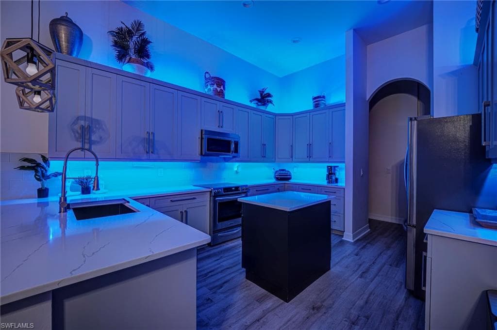 Kitchen featuring stainless steel appliances, pendant lighting, dark wood-type flooring, light stone countertops, and a kitchen island