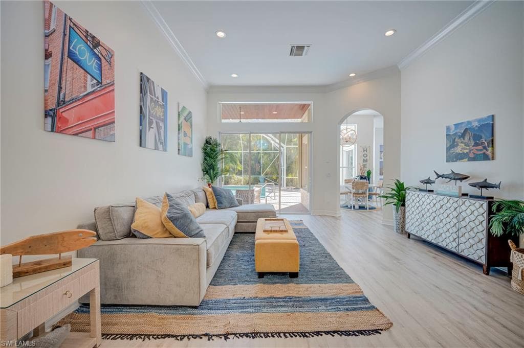Living area with arched walkways, crown molding, light wood-style floors, and recessed lighting