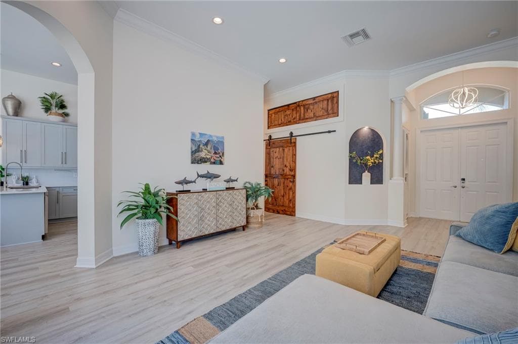 Living area with arched walkways, a barn door, light wood-style floors, crown molding, and recessed lighting