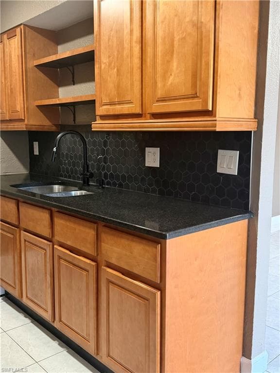 Kitchenette featuring wood-finish cabinetry, dark countertop, and a black hexagon tile backsplash