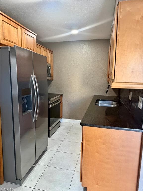 Kitchen featuring stainless steel appliances, light wood cabinetry, dark countertops, and tile flooring