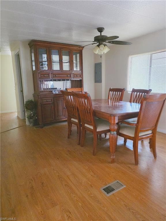 Dining room featuring light wood finished floors, a ceiling fan, and electric panel