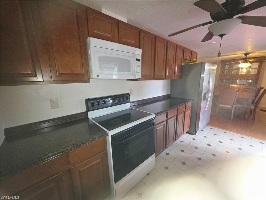 Kitchen with range with electric stovetop, white microwave, ceiling fan, light flooring, and wood finish cabinets