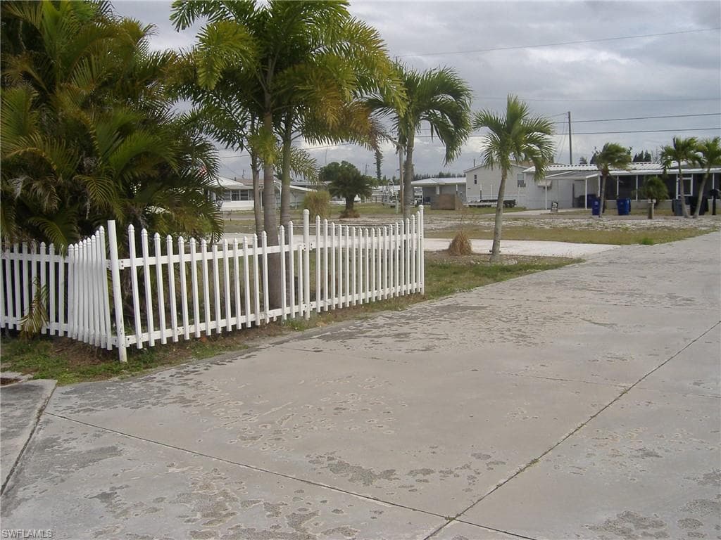 The property features a white picket fence, mature palm trees, and a concrete driveway