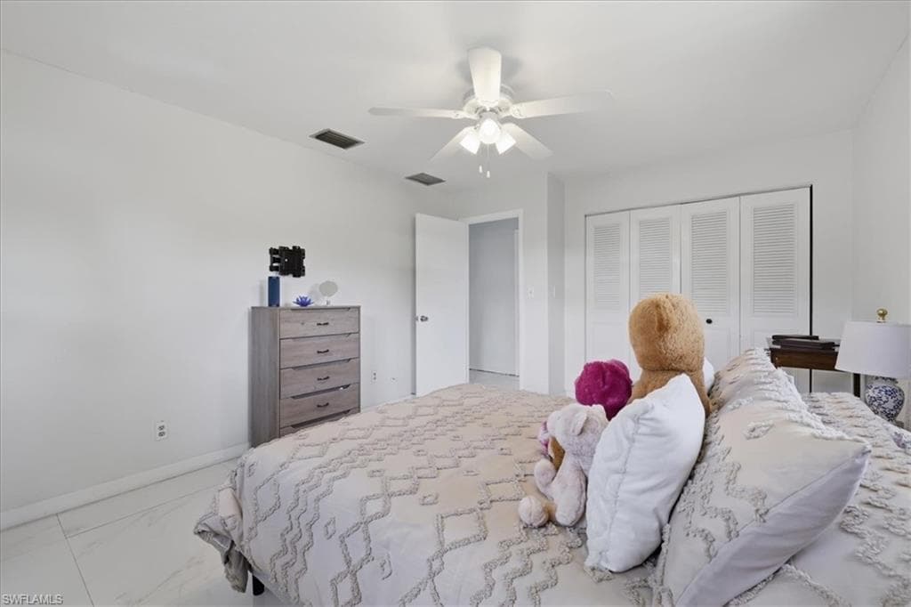 Bedroom with ceiling fan, light marble finish floors, and a closet