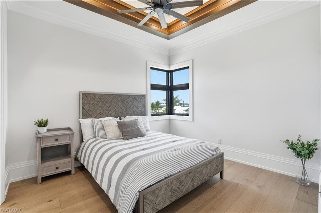 Bedroom with light wood-style floors, ornamental molding, a ceiling fan, and a raised ceiling - Virtually Edited Image