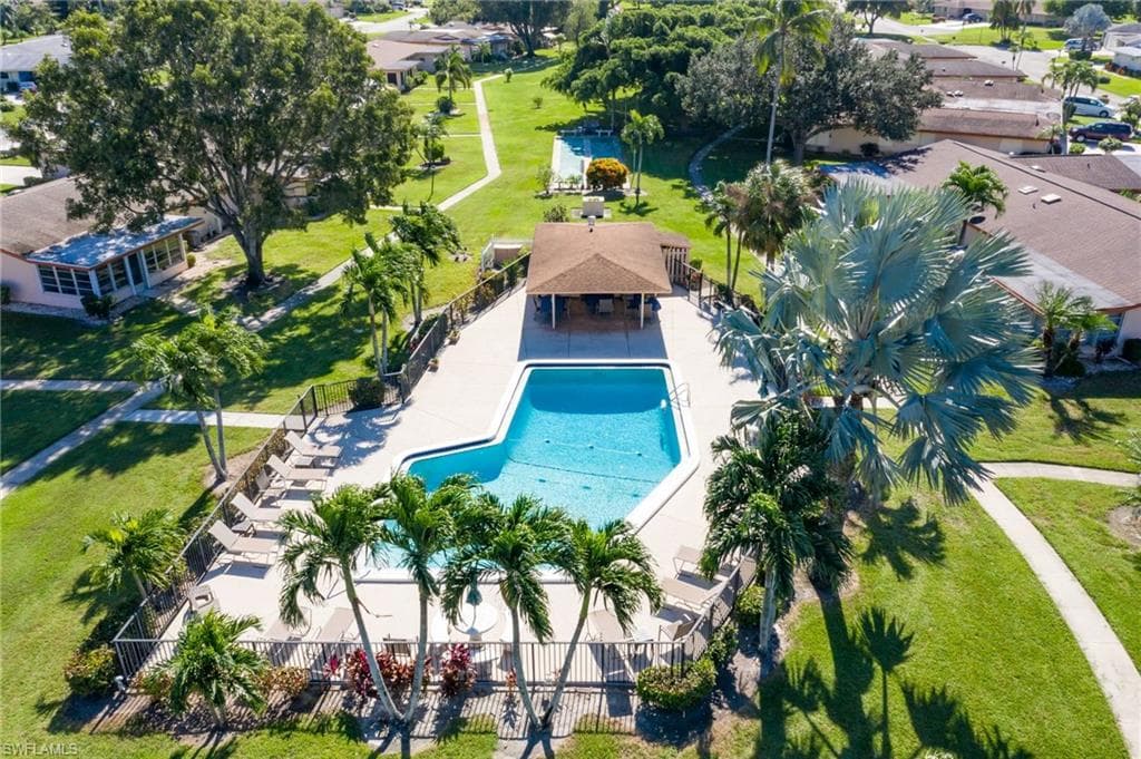 Fenced community pool with surrounding lounge chairs, shaded cabana area, and a large sun deck