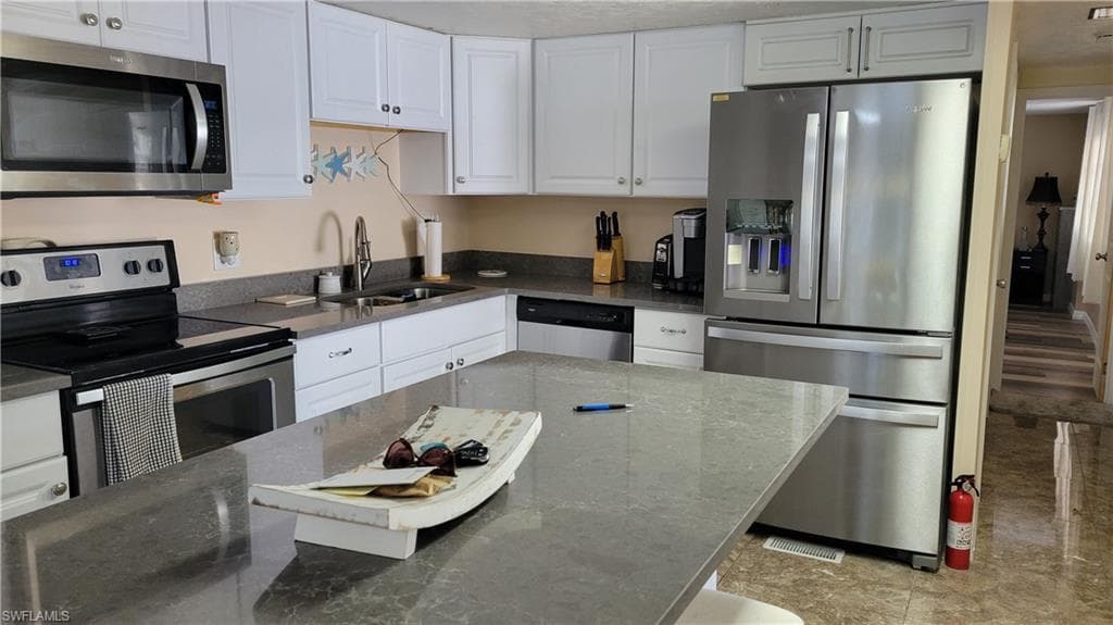 View of kitchen with stainless refrigerator, dishwasher, sink and island.