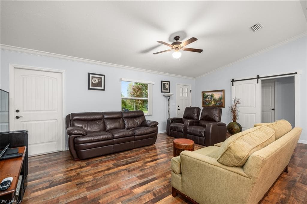 Living area with crown molding, a barn door, dark wood-style flooring, a ceiling fan, and vaulted ceiling