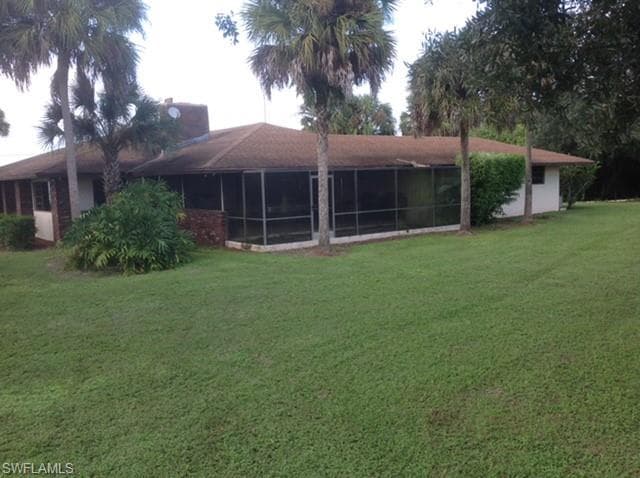 Rear view of property with a lawn, a chimney, and a sunroom