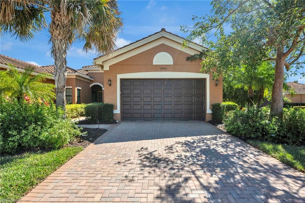 Front elevation with two-car garage and paver driveway framed by tropical landscaping.