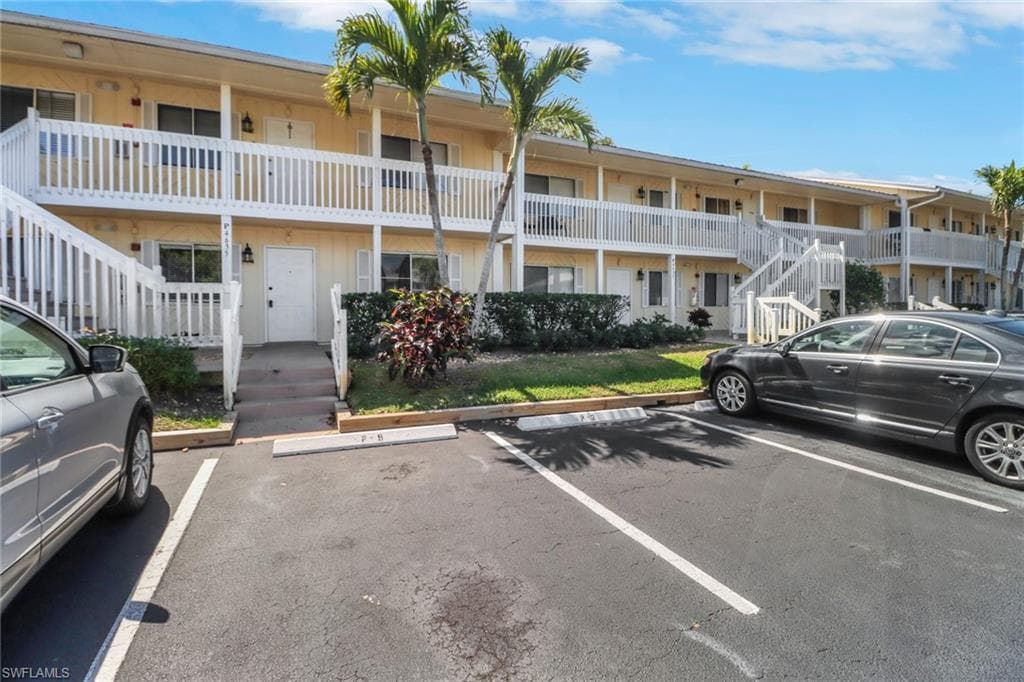 View of property with stairway and uncovered parking