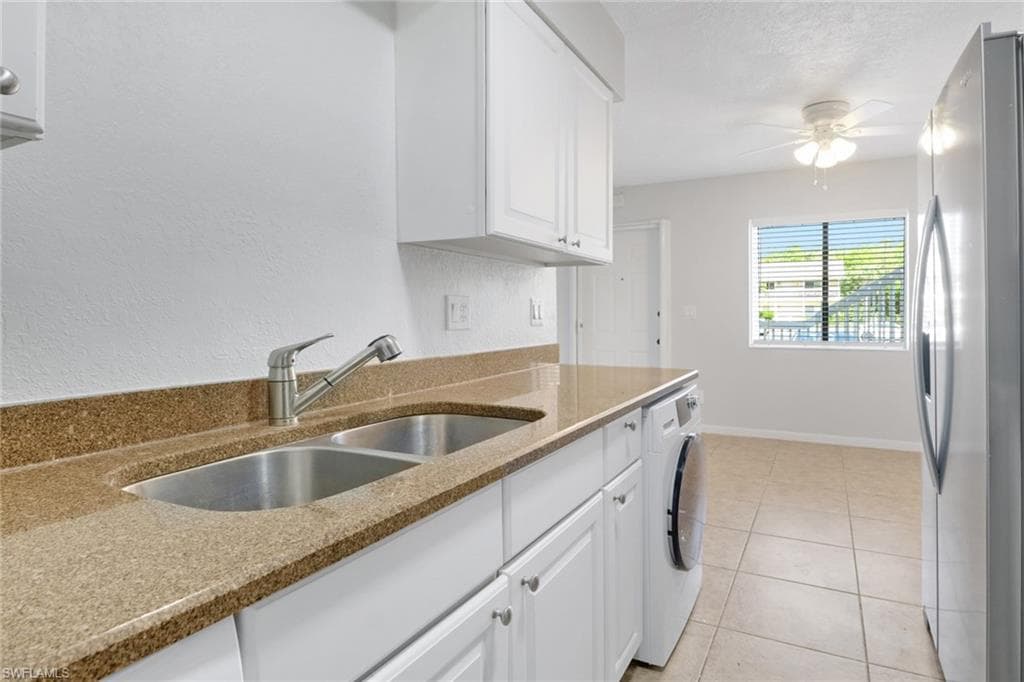 Kitchen with light tile patterned floors, washer / dryer, freestanding refrigerator, a sink, and white cabinetry