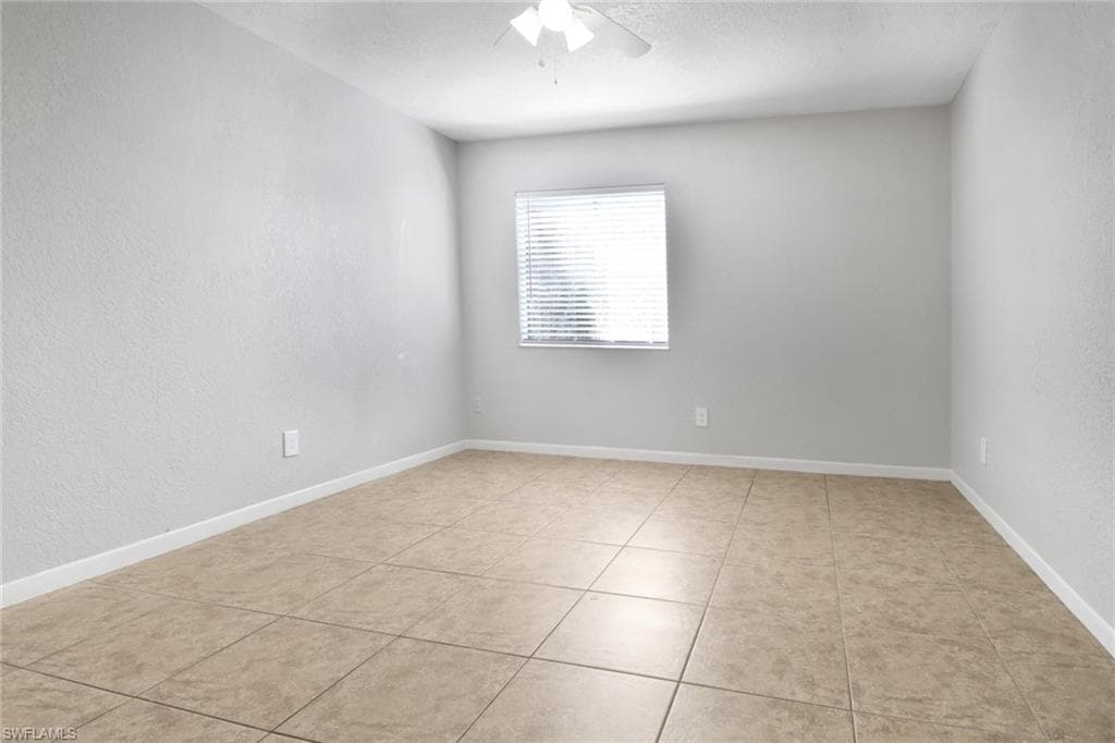 Spare room with light tile patterned floors, baseboards, and ceiling fan