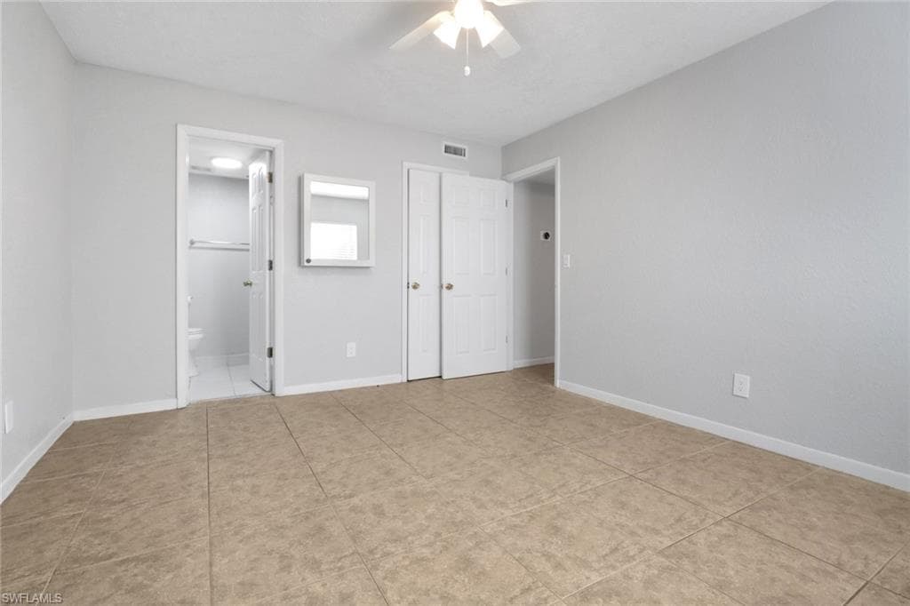 Unfurnished bedroom featuring visible vents, ensuite bathroom, light tile patterned floors, baseboards, and ceiling fan