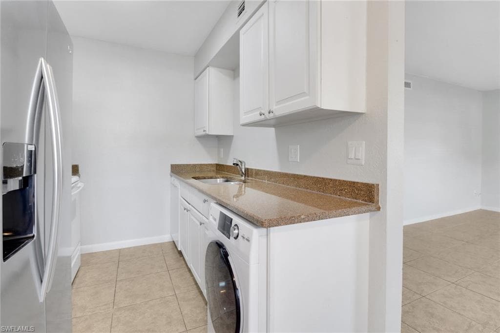 Kitchen with dark stone countertops, washer / dryer, stainless steel refrigerator with ice dispenser, white cabinetry, and a sink