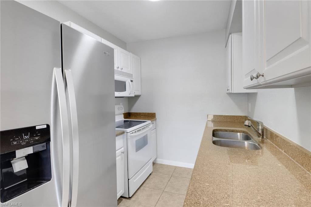 Kitchen with white appliances, light tile patterned floors, baseboards, a sink, and white cabinetry