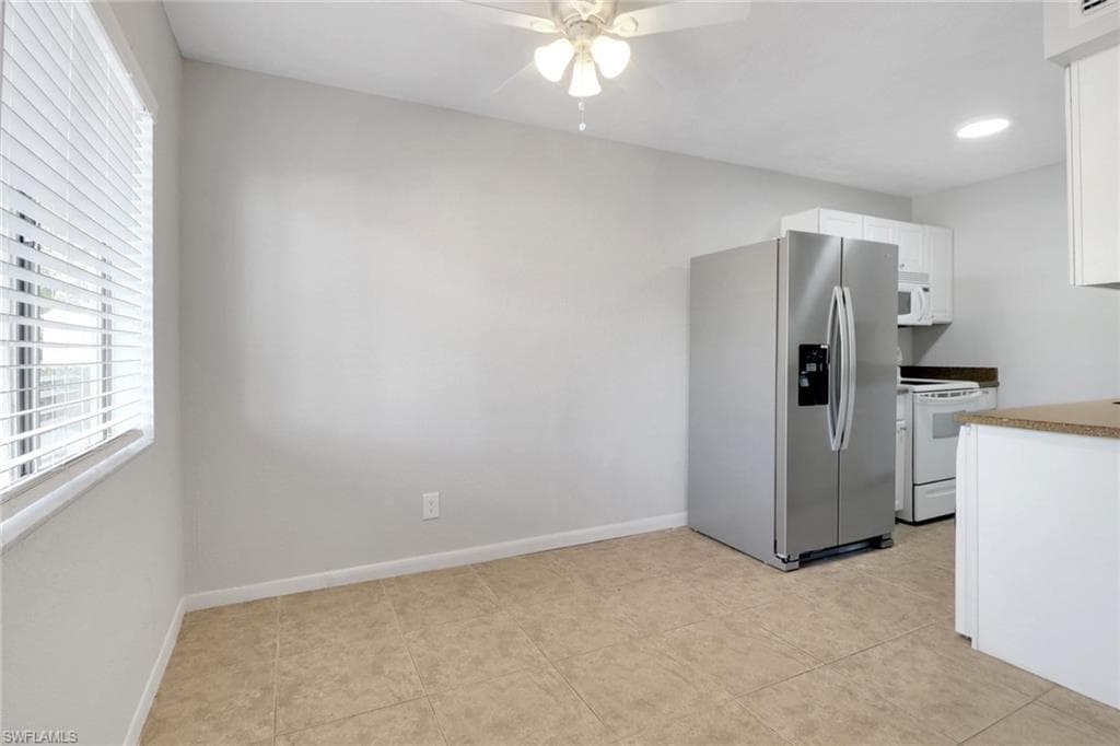 Kitchen featuring white appliances, white cabinets, a ceiling fan, and baseboards