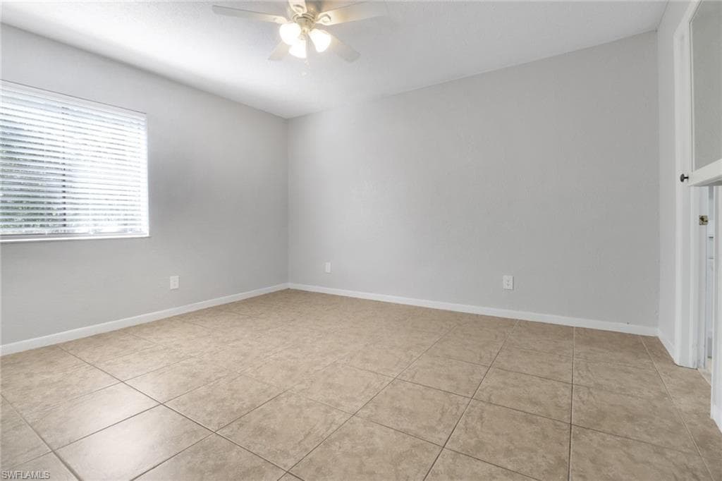 Empty room with light tile patterned floors, baseboards, and ceiling fan