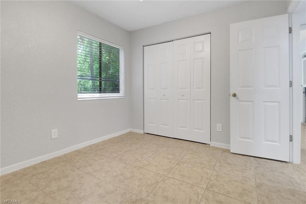 Unfurnished bedroom featuring a closet, light tile patterned floors, and baseboards